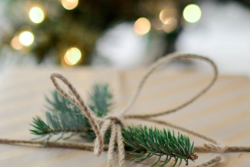 A piece of evergreen is tied onto a brown paper wrapped gift with a piece of twine
