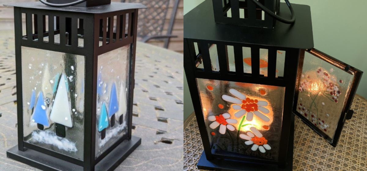 Two black lanterns side by side, one with a blue tree glass design and the other with orange flowers on the glass and a tea light lit inside with the door open