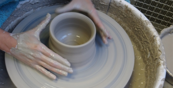 A pottery wheel spinning with a person shaping a pot with their hands