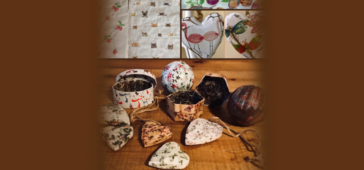 Handmade decoupage craft items, including decorated heart-shaped ornaments, small boxes, and spherical objects with floral and nature-inspired designs, displayed on a wooden surface.