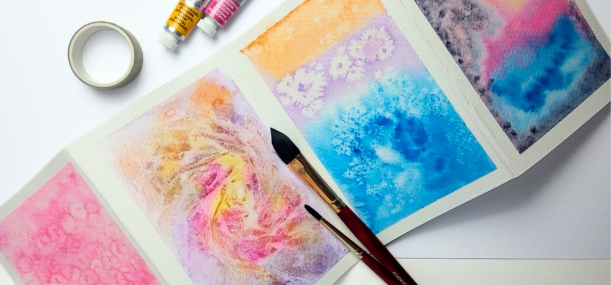 Two paintbrushes sit on top of 4 pastel watercolour pictures