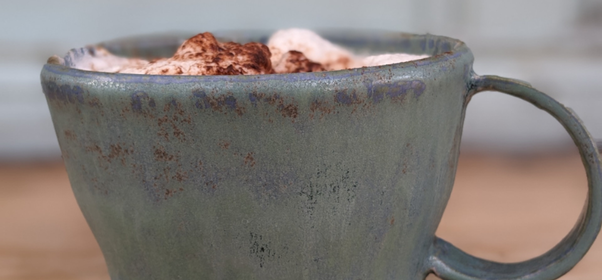 A grey handmade mug with cream and marshmallows in it.