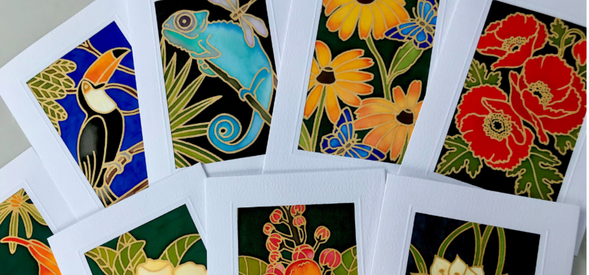 Hand-painted silk artwork greeting cards featuring colorful nature-inspired designs, including flowers, a toucan, a chameleon, and tropical plants.