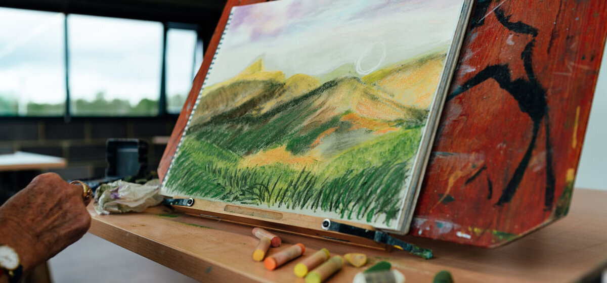A scenic pastel drawing on white paper, propped up on an easel