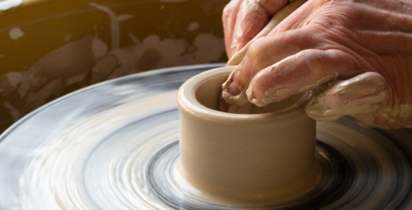 A potters wheel with hands throwing a pot in clay
