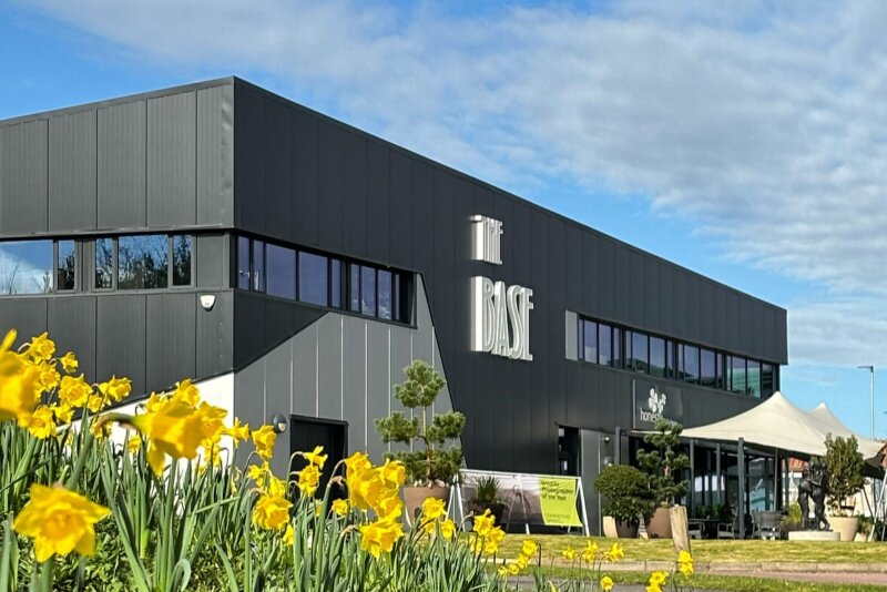 There are daffodils in the foreground and a black and grey modern building with a row of windows and sign saying 'The Base'.