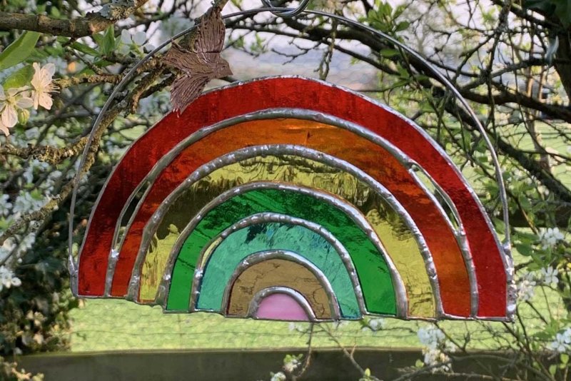 A rainbow glass hanging from a tree with a green rural landscape in the background