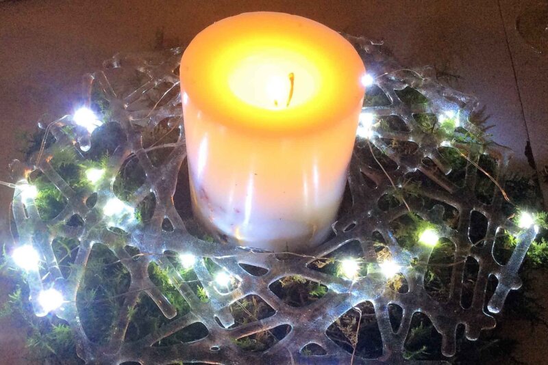 A candle in the centre of a Christmas wreath made with glass.