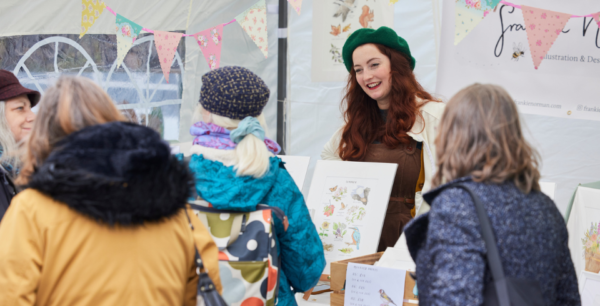 A group of being at a crafts festival looking at a stall holders artwork